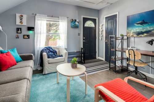Cozy living room with a sofa, desk, and colorful decor, featuring a door and large window with natural light.