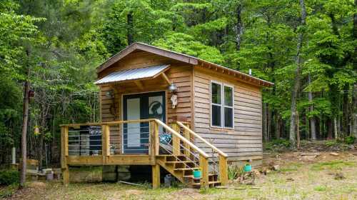 A small wooden cabin with a porch, surrounded by lush green trees in a serene forest setting.