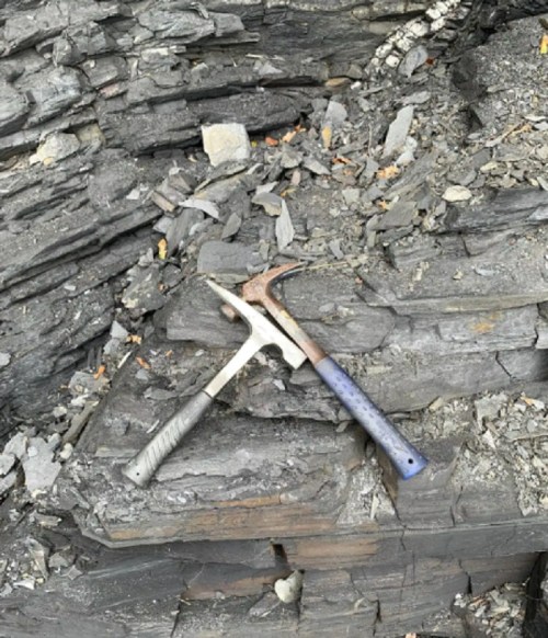 Two geological hammers resting on layered rock formations.