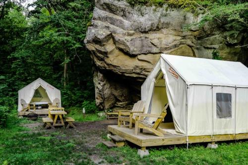 Two white canvas tents on wooden platforms near a rocky cliff, surrounded by lush greenery.
