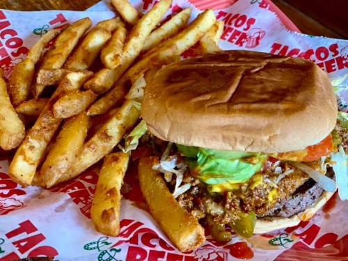 A hearty burger topped with lettuce, tomato, and avocado, served with crispy French fries on a red and white paper backdrop.