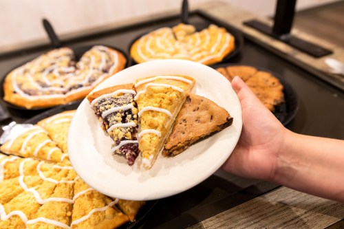 A hand holds a plate with three slices of dessert: fruit-topped, crumbly, and chocolate chip cookie.