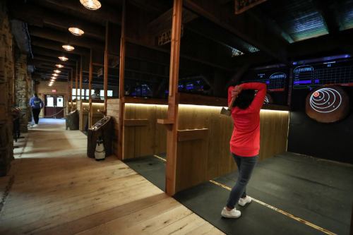 A person in a red shirt prepares to throw an axe at a target in a rustic indoor axe-throwing venue.
