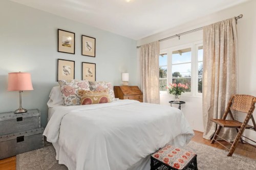 Cozy bedroom with a white bed, decorative pillows, framed bird art, and natural light from a window.