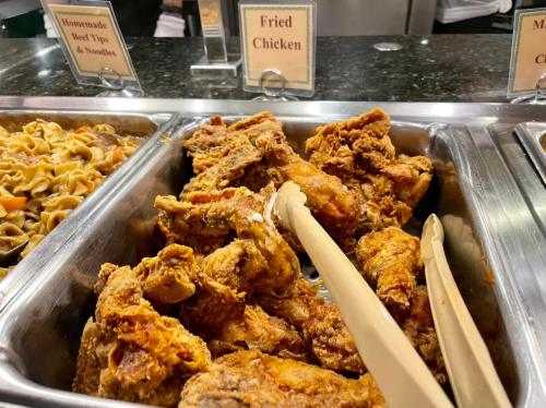A tray of crispy fried chicken pieces with tongs, displayed in a buffet setting.