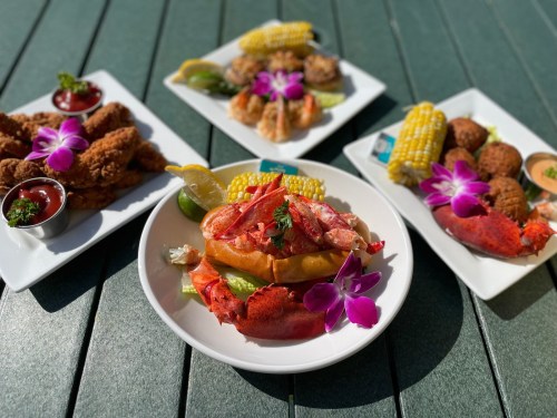 A plate of lobster roll garnished with flowers, surrounded by fried chicken, shrimp, and corn on the cob.