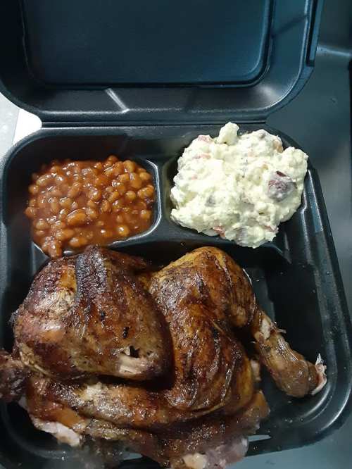 A takeout container with grilled chicken, baked beans, and potato salad.