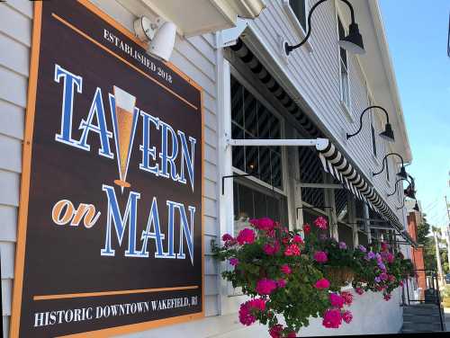 Sign for "Tavern on Main" in historic downtown Wakefield, RI, featuring flowers and a welcoming exterior.