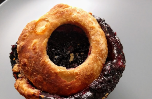 A close-up of a baked pastry with a hollow center filled with dark fruit filling, resting on a gray plate.