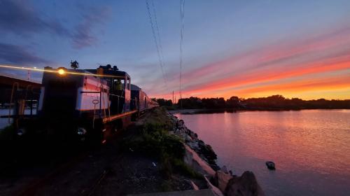 A train parked by a river at sunset, with vibrant colors reflecting in the water and a serene landscape.