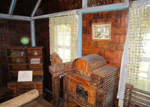 Interior of a rustic room featuring wooden furniture, a globe, and decorative curtains, with a vintage photo on the wall.