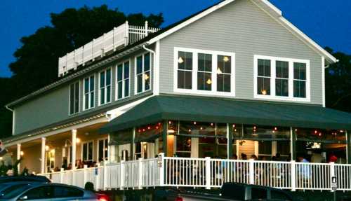 A cozy restaurant with large windows and outdoor seating, illuminated at dusk.