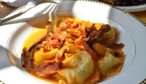 A plate of ravioli in a creamy tomato sauce, topped with mushrooms and sun-dried tomatoes, served in a decorative bowl.