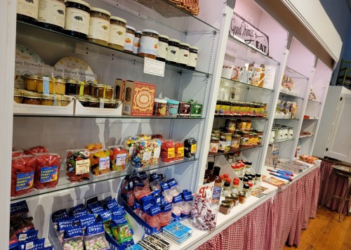 A colorful display of jars, candies, and spreads on shelves in a quaint store, with a checkered tablecloth below.
