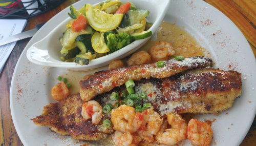A plate of fried fish fillets topped with shrimp and green onions, served with a side of sautéed vegetables.