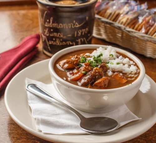 A bowl of hearty stew with rice, garnished with parsley, next to a can and a basket of cookies.