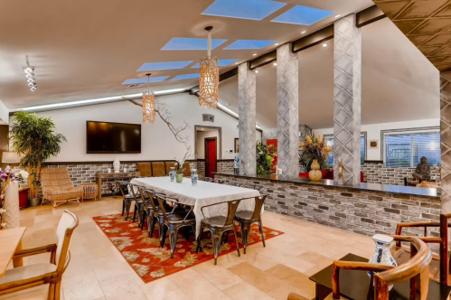 A spacious, modern dining area with a long table, decorative plants, and stylish lighting fixtures.
