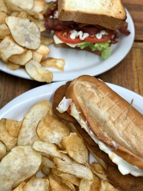A plate of crispy potato chips alongside a sandwich with bacon, lettuce, tomato, and mayonnaise on toasted bread.