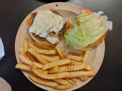 A plate with a burger topped with cheese, lettuce, and tomato, accompanied by a side of crinkle-cut fries.