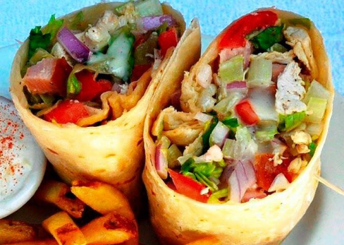 Two wrapped burritos filled with chicken, lettuce, tomatoes, and onions, served with fries on the side.