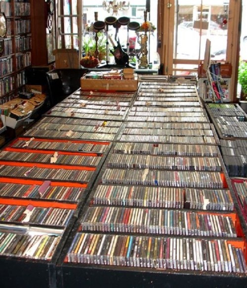 A large table filled with neatly organized CDs in a cozy shop, with shelves and decor in the background.