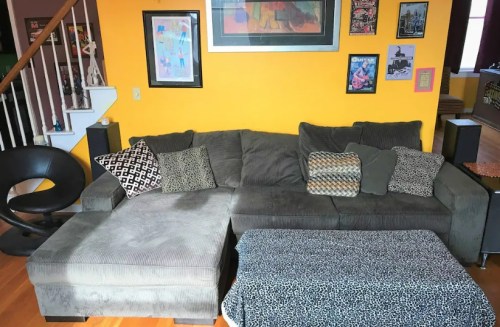 A cozy living room featuring a gray sectional couch with patterned pillows, a coffee table, and colorful wall art.