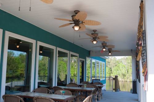 Outdoor dining area with ceiling fans, tables, and large windows overlooking a green landscape.