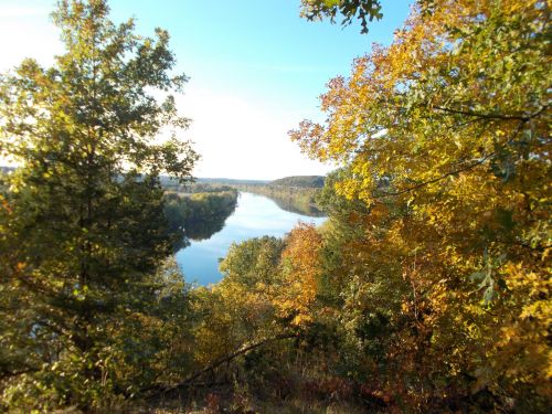A serene river flows through a landscape of vibrant autumn foliage under a clear blue sky.