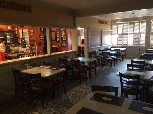 A cozy restaurant interior with empty tables, patterned flooring, and warm lighting.