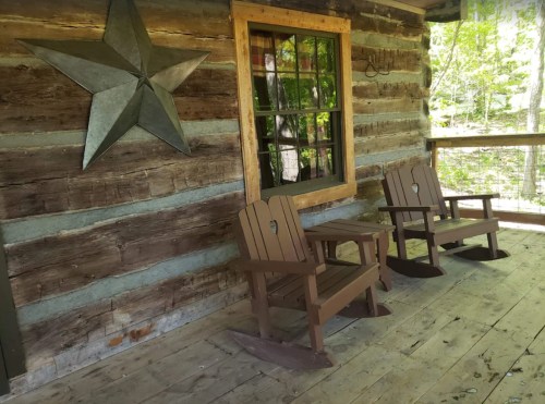 Two wooden rocking chairs on a porch in front of a log cabin, with a star decoration and a window nearby.