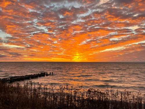 Sunset over a calm lake, with vibrant orange and yellow hues reflecting on the water and a cloudy sky above.