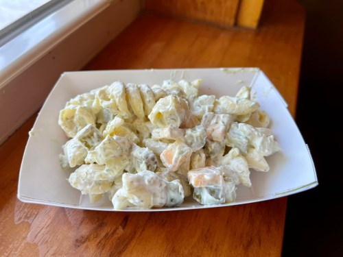 A white plate filled with creamy pasta salad, featuring small pasta pieces and mixed vegetables.