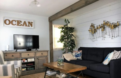 Cozy living room with a TV, a wooden coffee table, plants, and ocean-themed decor on the walls.