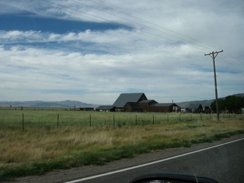 A rural landscape featuring a barn and farmhouse, with open fields and mountains under a cloudy sky.