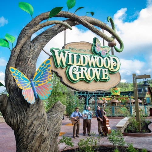 A whimsical sign reading "Welcome to Wildwood Grove" with musicians playing nearby, surrounded by trees and butterflies.