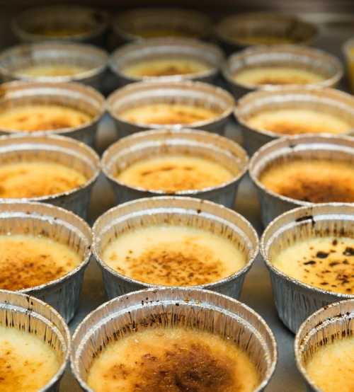 A close-up of multiple small aluminum cups filled with a creamy dessert, each with a caramelized top.