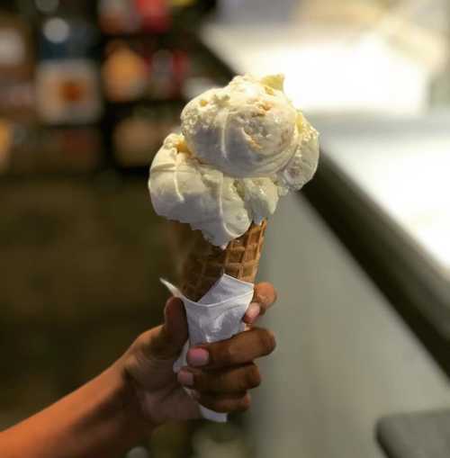 A hand holding a cone with two scoops of creamy vanilla ice cream.