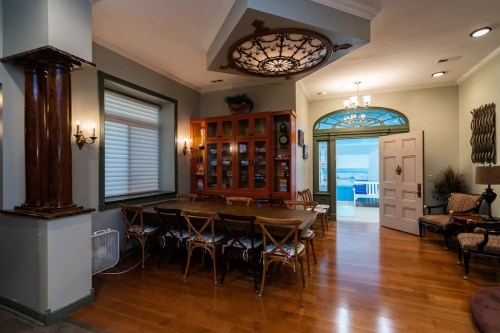 A spacious dining area with a large table, wooden floors, and decorative lighting, leading to an outdoor view.