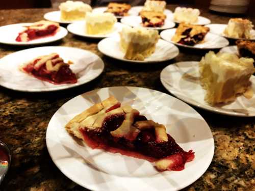 Slices of pie on white plates, featuring berry filling and a lattice crust, arranged on a granite countertop.