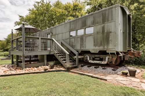 A vintage train car converted into a unique outdoor space, surrounded by greenery and a stone pathway.