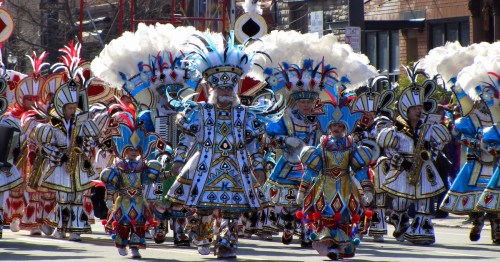 A vibrant parade featuring performers in colorful costumes with feathers, marching down a city street.