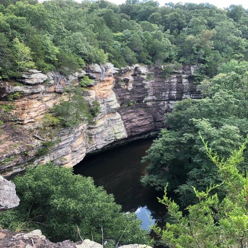 A serene view of a rocky canyon surrounded by lush green trees and a calm river flowing through the bottom.