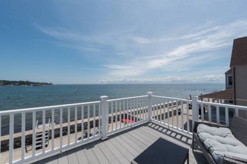 A scenic view of a calm waterfront from a deck, featuring blue skies and distant clouds over the water.