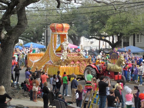 A colorful parade float adorned with gold and vibrant decorations, surrounded by cheering crowds and festive atmosphere.