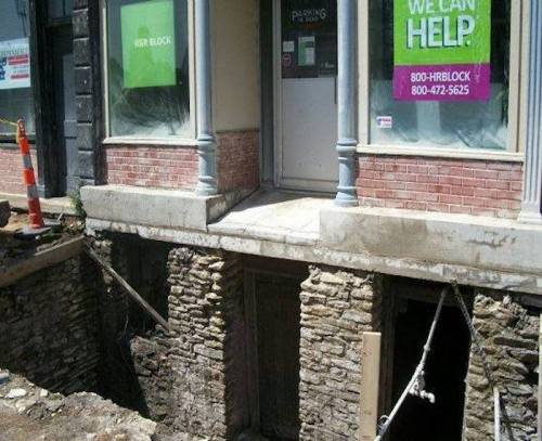 A building with a partially exposed basement, showing stone walls and construction barriers outside.