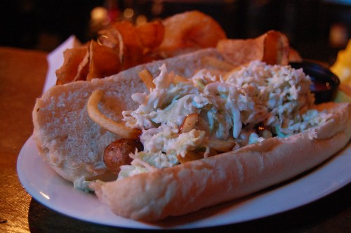 A plate featuring a sandwich filled with coleslaw and fried onions, accompanied by crispy potato chips.