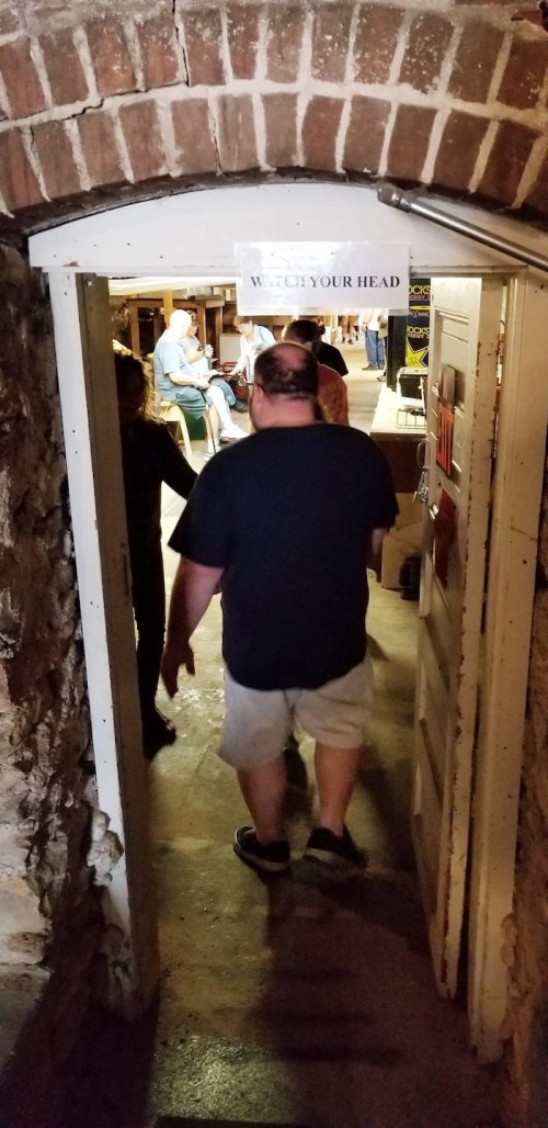 A person walks through a low doorway with a "Watch Your Head" sign, leading into a dimly lit room.