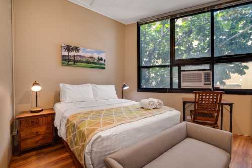 Cozy hotel room with a double bed, desk, and large window overlooking greenery. Warm tones and simple decor.