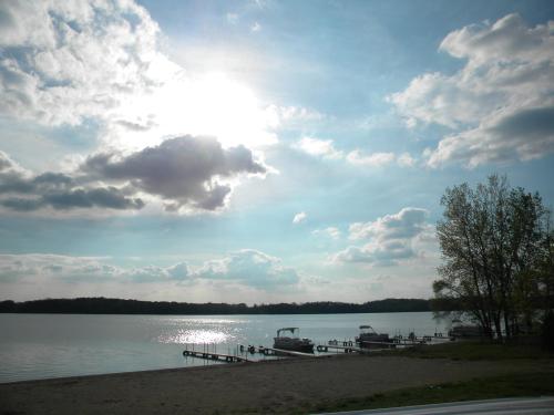 A serene lake scene with boats docked, under a cloudy sky and bright sun reflecting on the water.