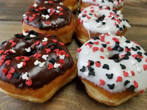 A close-up of donuts with chocolate and white icing, topped with red, black, and white sprinkles in heart shapes.